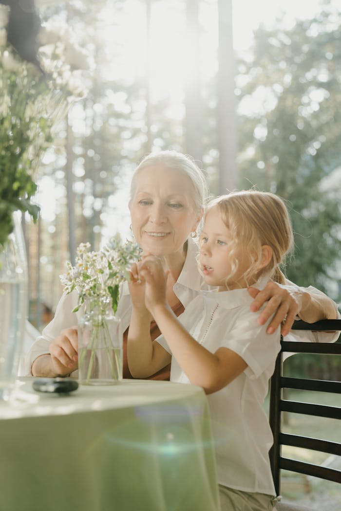A loving grandmother and granddaughter bond over flowers in a sunlit garden setting.